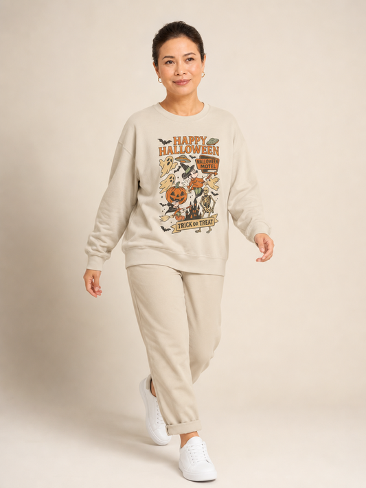 A woman modeling a beige crewneck sweatshirt and matching sweatpants set. The sweatshirt features a colorful 'Happy Halloween' graphic on the front with pumpkins, a witch, and ghosts.