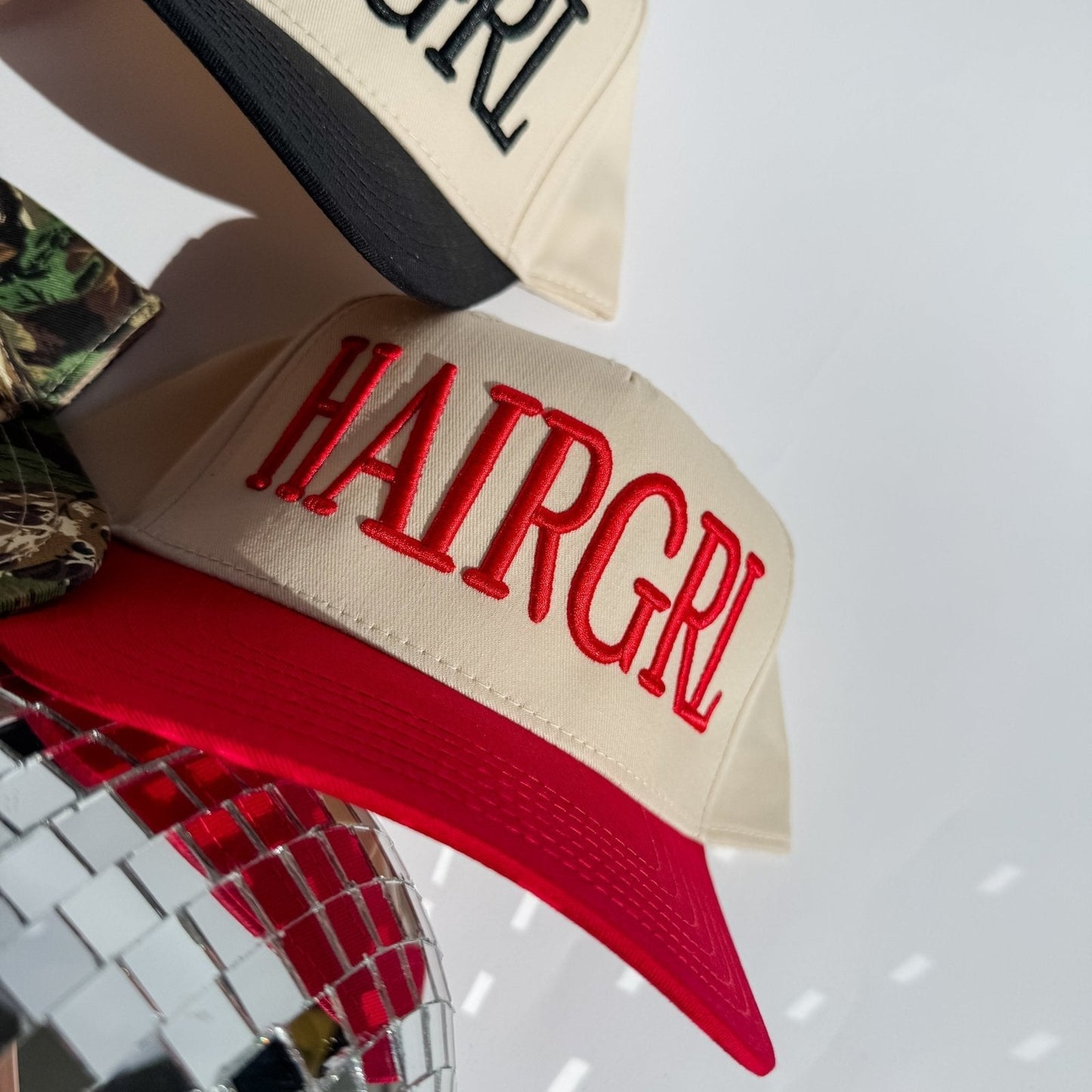 HAIRGRL - Trucker Hat with cream front and red bill, featuring bold red 3D puff embroidery and adjustable snapback closure.