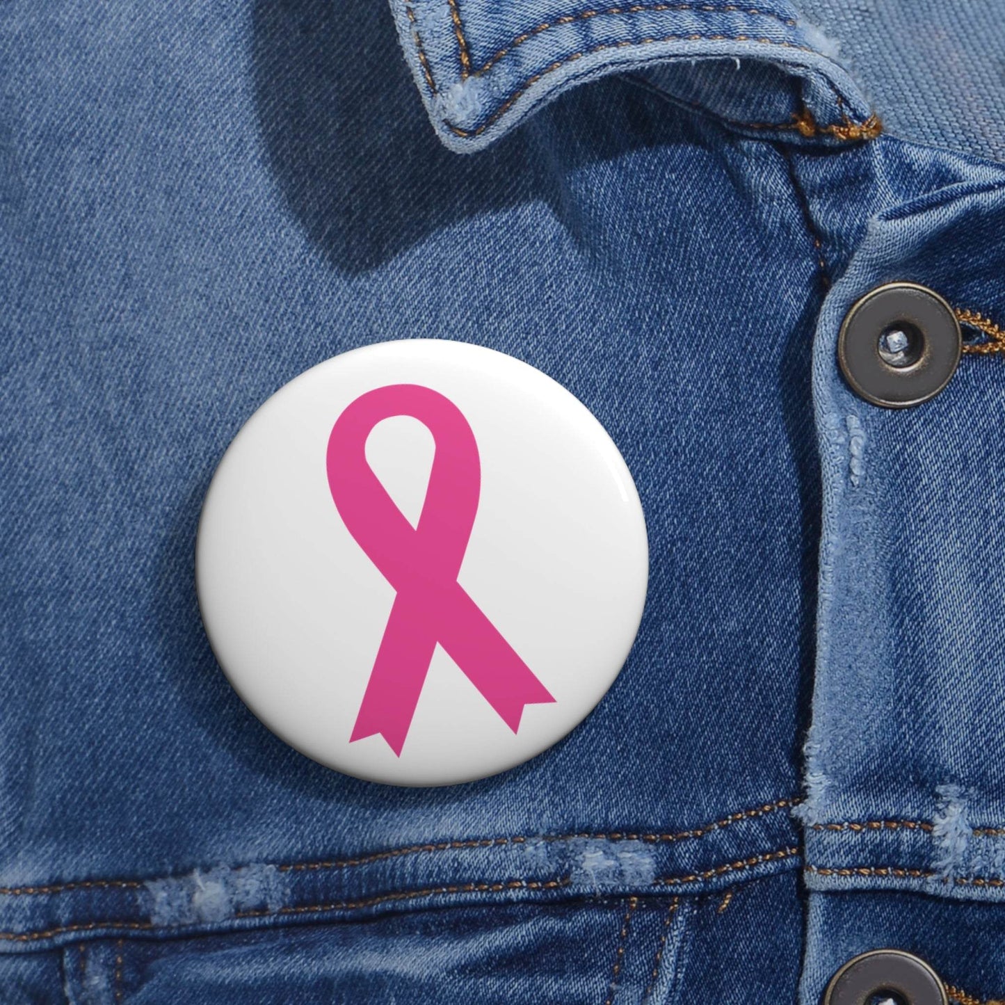 Pink Awareness Ribbon Pin button with a glossy finish and vibrant pink ribbon design on a white background pinned to blue denim fabric