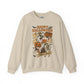 A beige crewneck sweatshirt featuring a colorful retro Halloween graphic on the front with the text 'Happy Halloween' and 'Trick or Treat' along with illustrations of a pumpkin, ghosts, a skeleton, and a motel sign.