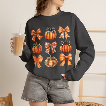 A woman wearing a darker gray crewneck sweatshirt with a graphic print of orange pumpkins and plaid bows, holding an iced coffee in a cafe setting.