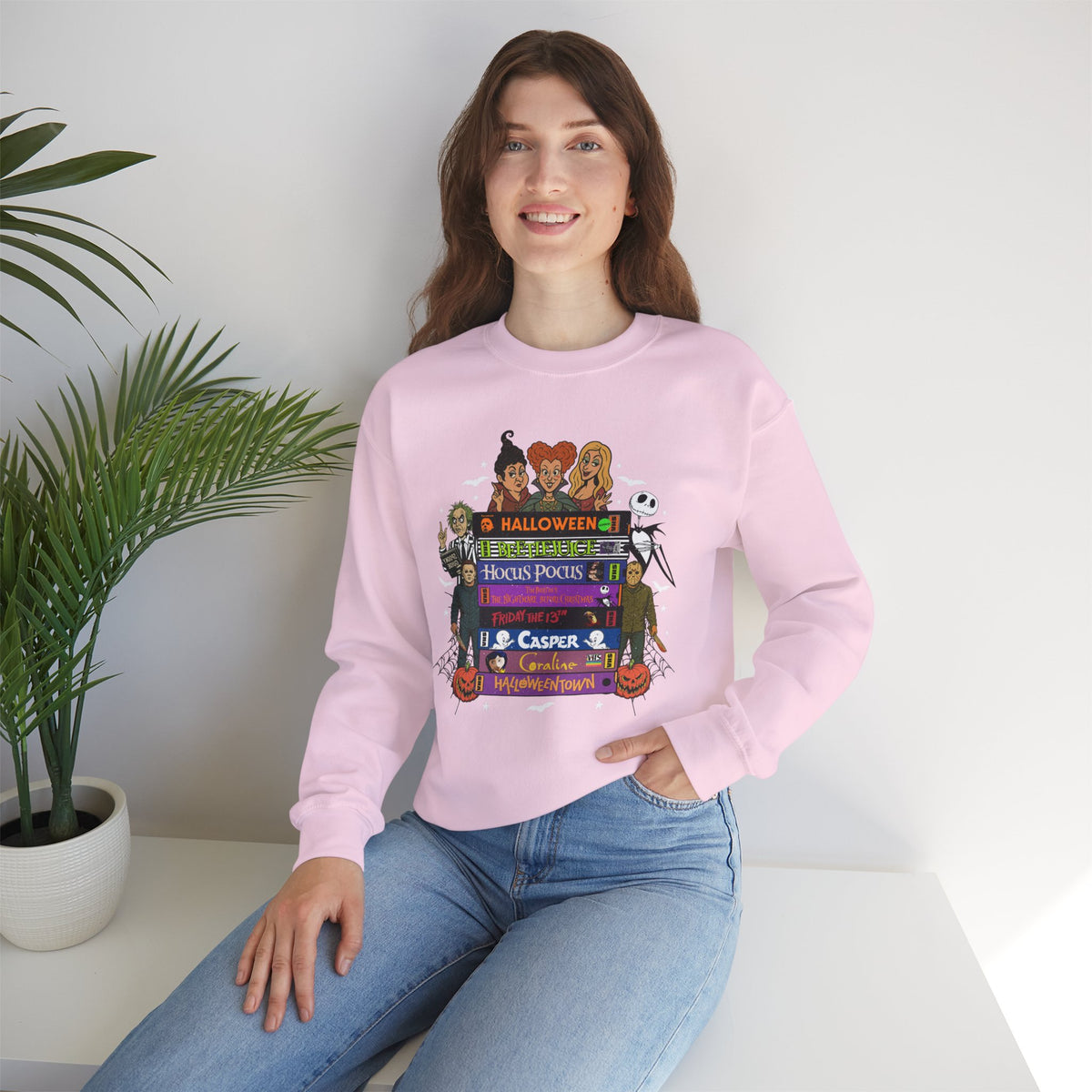 A woman wearing a light pink crewneck sweatshirt with a colorful graphic print of 'spooky movies'