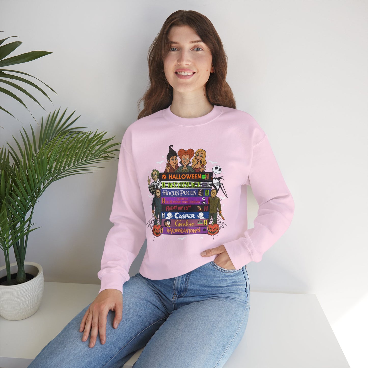 A woman wearing a light pink crewneck sweatshirt with a colorful graphic print of 'spooky movies'