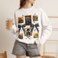 Woman wearing a white crewneck sweatshirt featuring a vintage witch-themed Halloween collage with black bows, bats, pumpkins, and orange accents.
