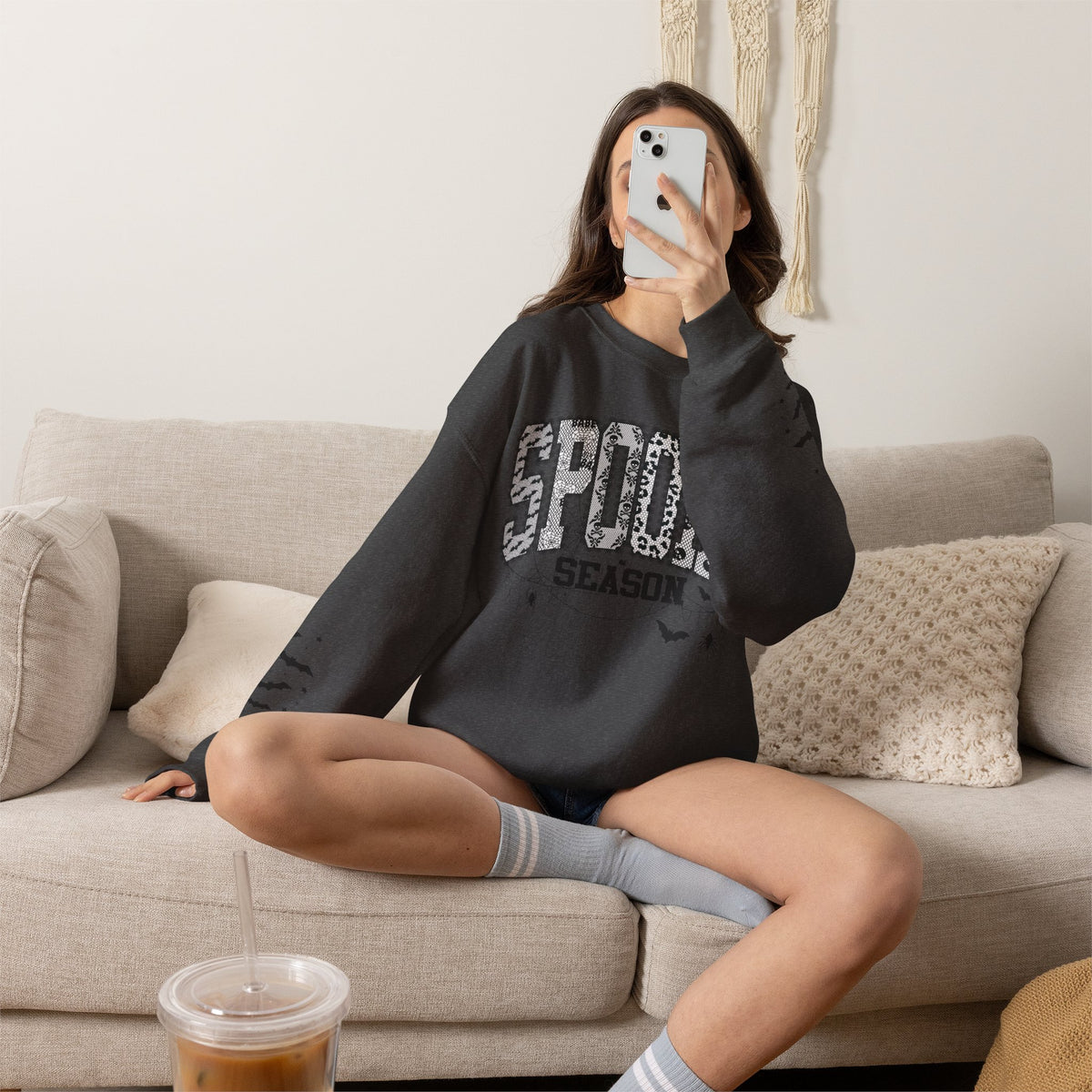 Woman wearing a black sweatshirt with text, sitting on a couch in a living room.