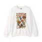 An white crewneck sweatshirt featuring a colorful 'Happy Halloween' graphic print on the front with illustrations of a witch, skeleton, ghost, and a jack-o'-lantern.