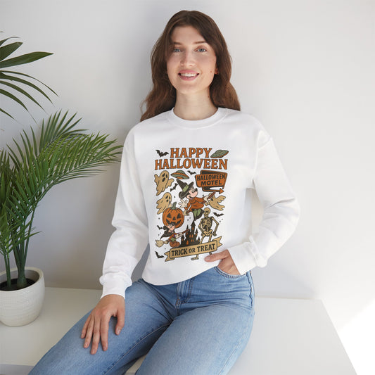 A woman wearing a white long-sleeve crewneck sweatshirt with a colorful 'Happy Halloween' graphic print, paired with blue jeans, sitting in a bright room next to a potted plant.