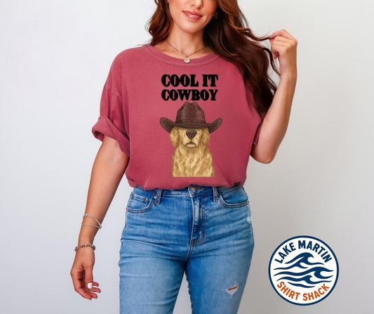 Person wearing a t-shirt with a graphic of a dog wearing a cowboy hat and text 'Cool It Cowboy', standing against a plain background with Lake Martin Shirt Shack logo.