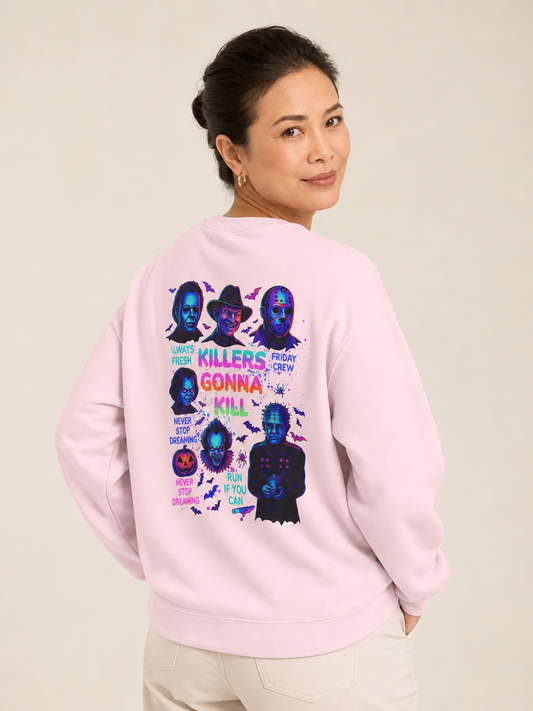 Woman modeling the back of a light pink crewneck sweatshirt featuring a colorful “Killers Gonna Kill” horror-character graphic.