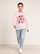 A woman modeling a light pink crewneck sweatshirt with a 'spooky graphic featuring cartoon ghost and stars