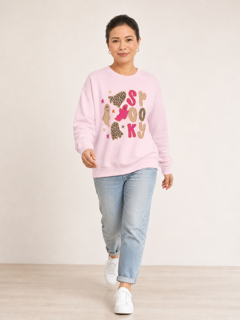 A woman modeling a light pink crewneck sweatshirt with a 'spooky graphic featuring cartoon ghost and stars