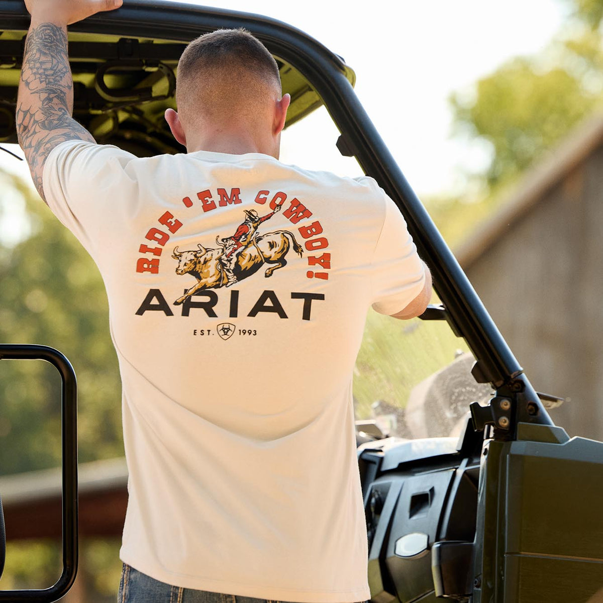 Ariat Mens Short Sleeve Shirt in cream cotton with bold red and black "Ride Em Cowboy" graphic and Ariat branding on back.