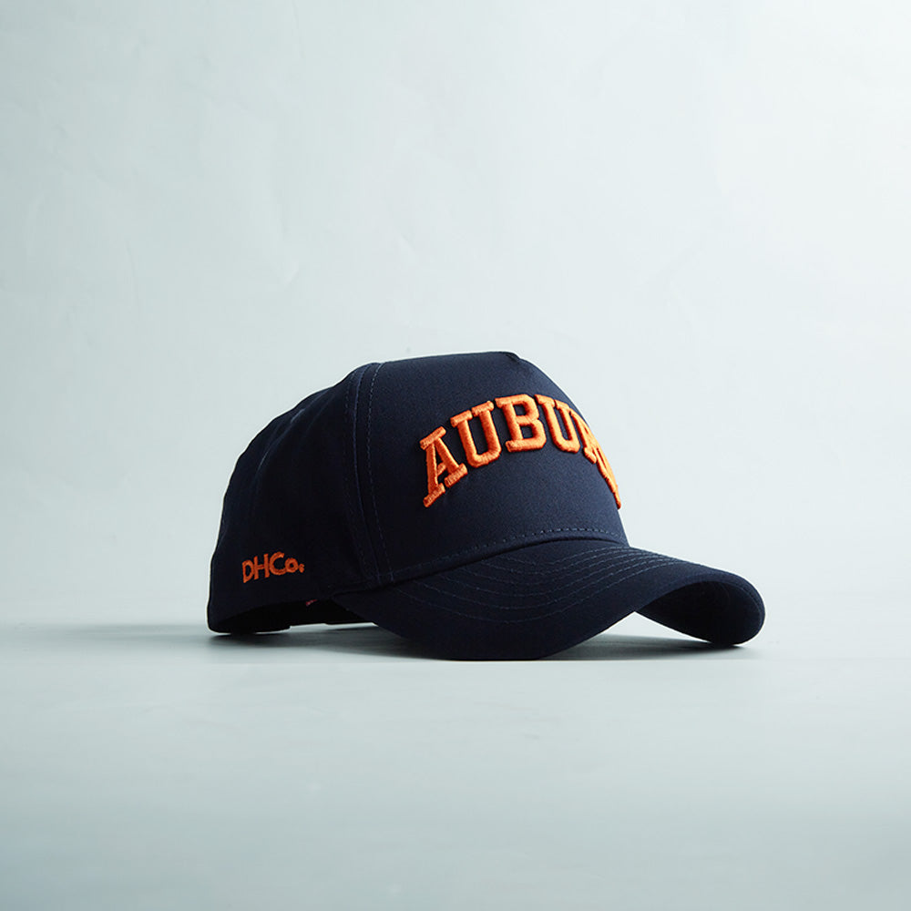 Navy blue structured snapback hat with bold orange 3D "AUBURN" embroidery and side stitching, representing Auburn Alabama Legacy.