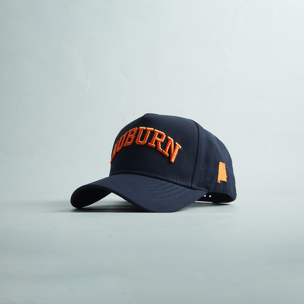 Navy blue structured snapback cap with curved bill, bold orange 3D "AUBURN" embroidery and Alabama state silhouette, featuring Auburn Alabama Legacy design.