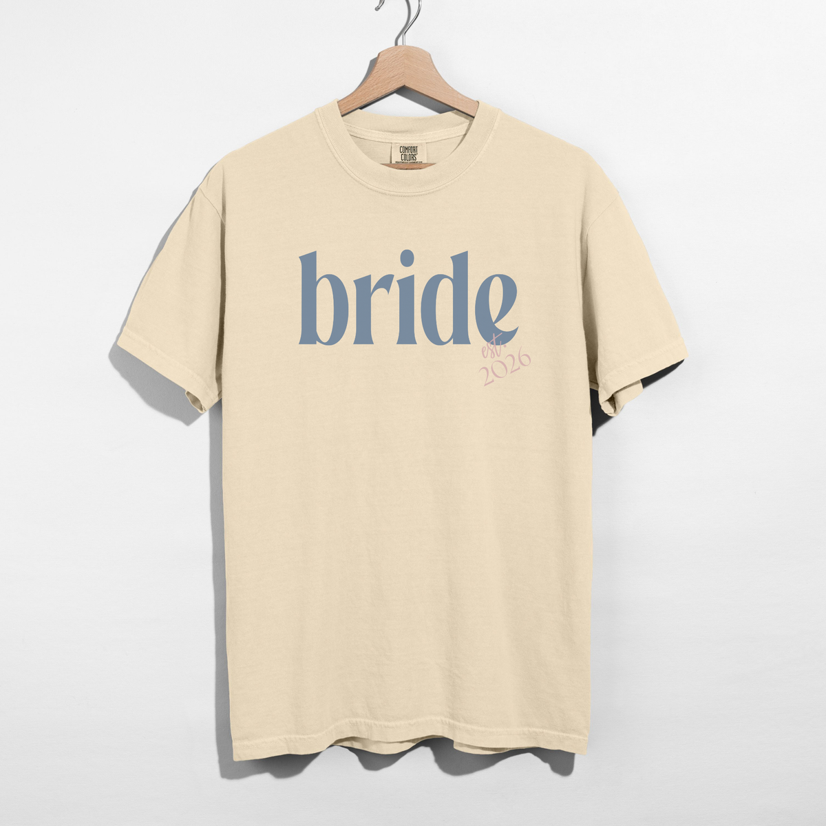 Bride Est. 2026 tee in cream cotton with blue serif bride lettering and pink 2026 detail
