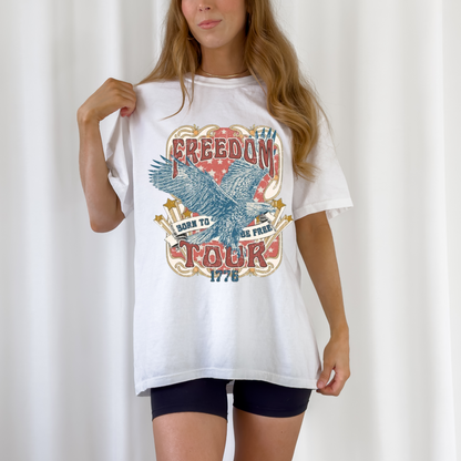 Freedom Tour Tee in white cotton with a vintage patriotic eagle graphic and bold red and blue text detailing 1776