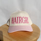 HAIRGRL - Trucker Hat with cream front, pink bill, and raised pink embroidery spelling "HAIRGRL" on the front panel