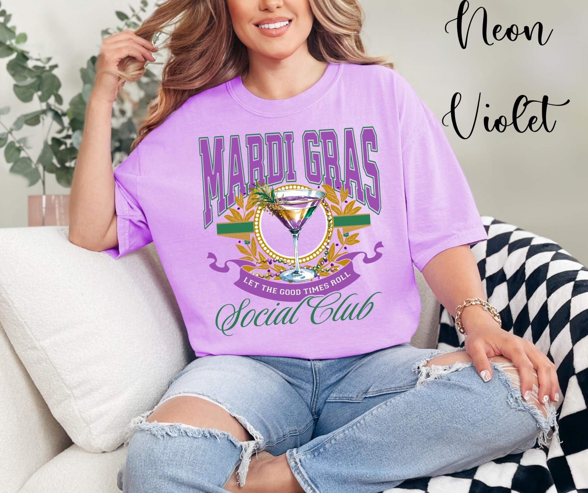 Person wearing a purple 'Mardi Gras Social Club' t-shirt sitting on a couch.