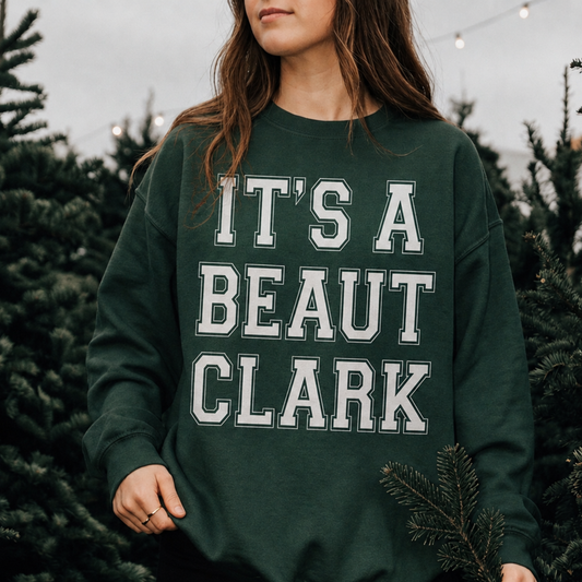 It's a Beaut Clark Christmas Sweatshirt in forest green with bold white collegiate lettering and a crewneck design