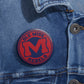 Ole Miss Rebels M Logo Pin in red and navy blue on a metal pin button attached to blue denim fabric