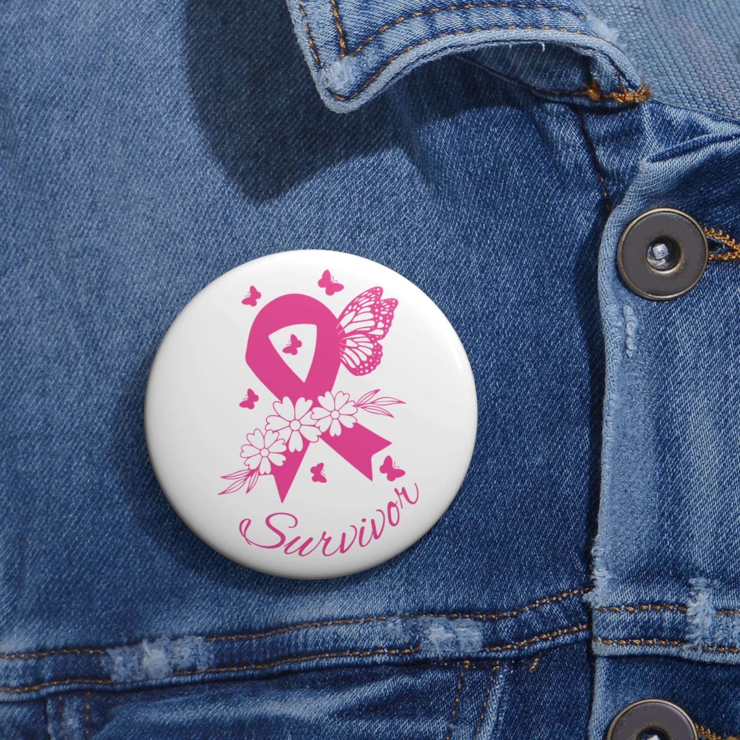 Pink Ribbon Survivor Pin featuring a bright pink awareness ribbon with floral and butterfly accents on a white round button pinned to blue denim fabric