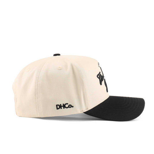 Pre-curved Trucker hat in beige and black with a structured crown, curved brim, and embroidered side branding