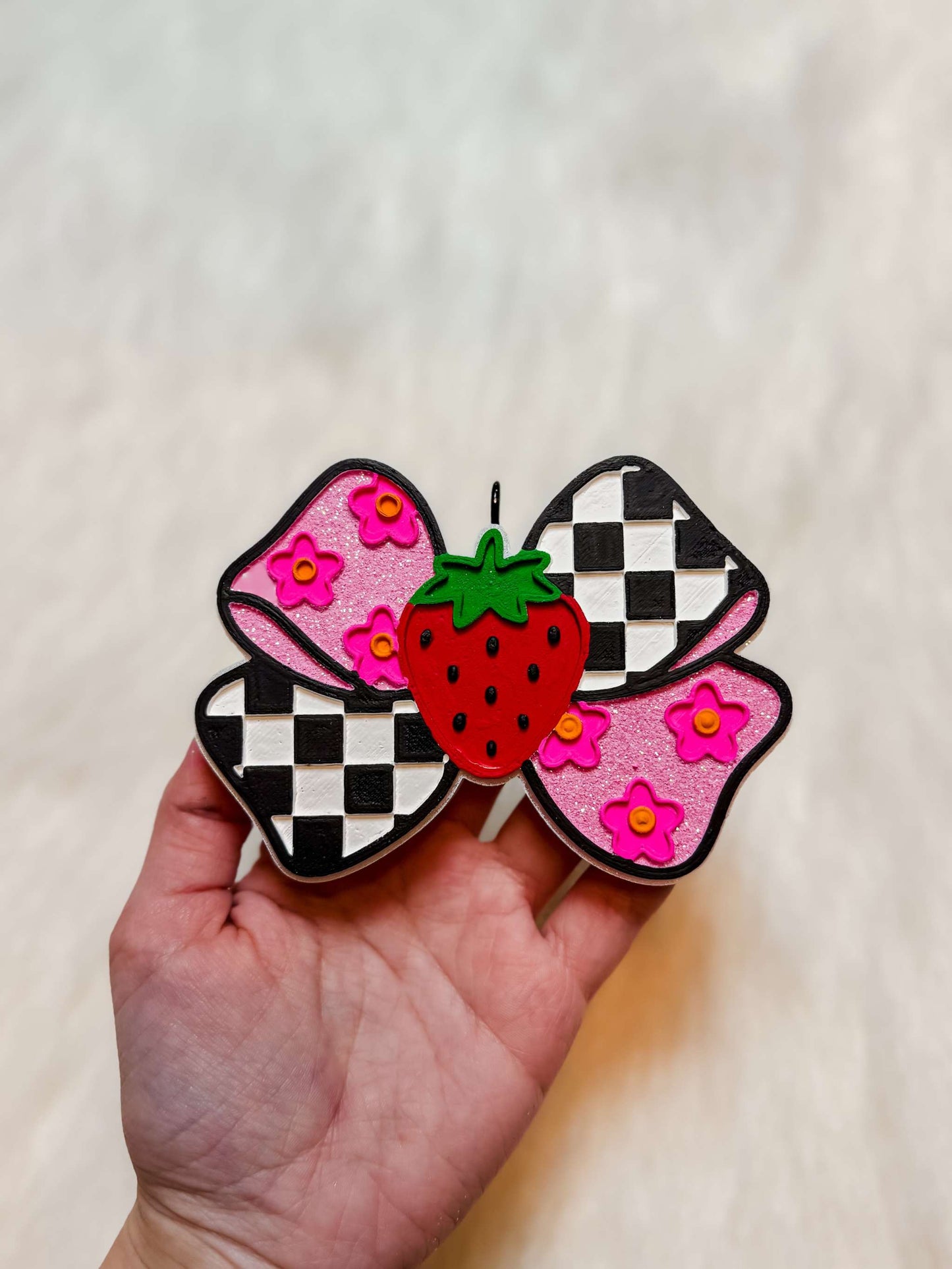 Strawberry Bow Freshie with pink and black checkerboard wings, pink floral pattern, and a red strawberry center