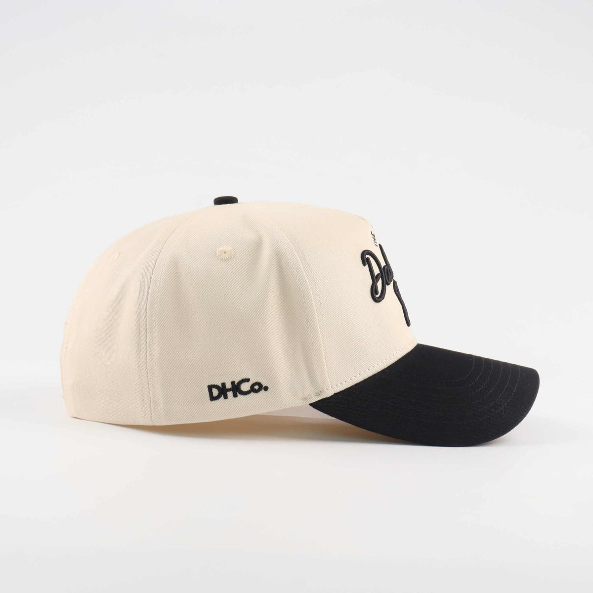 The Dallas Script Hat in beige canvas with a black pre-curved brim and embroidered script detail