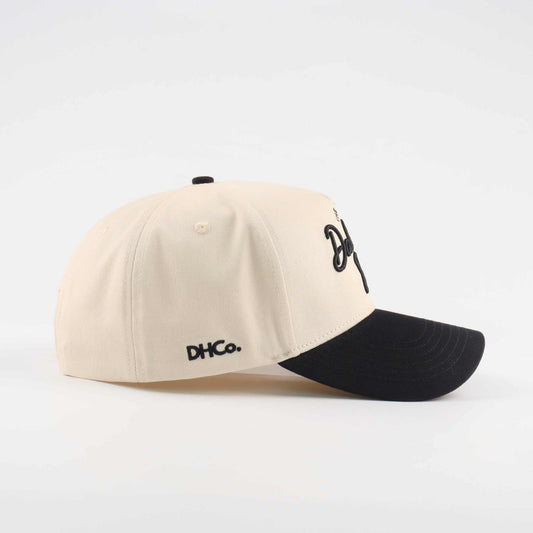 The Dallas Script Hat in beige canvas with a black pre-curved brim and embroidered script detail