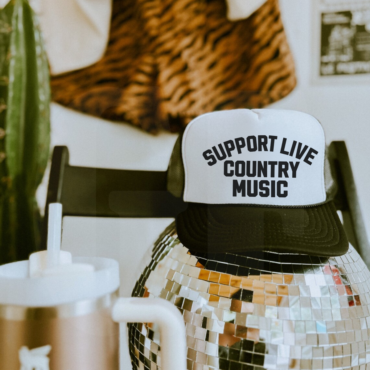 White and black trucker hat with mesh back and bold text saying Support Live Country Music on foam front panel